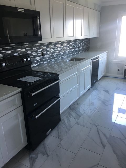 White kitchen with black appliances, mosaic backsplash, and marble-look flooring.