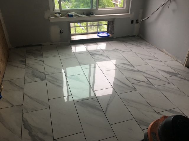 Room with newly tiled floor, white marble-look tiles. Gray walls, window with natural light.