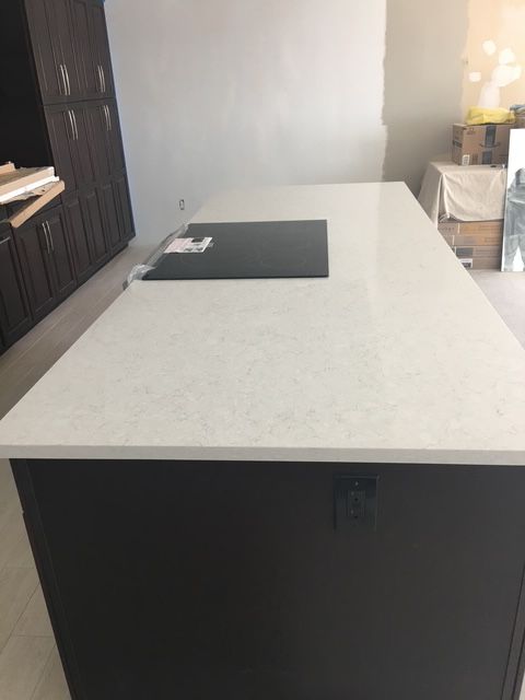 Dark brown kitchen island with a white countertop and black stovetop.