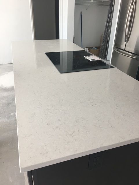 White quartz countertop with built-in black stovetop, in a modern kitchen setting.