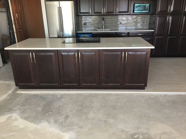 Dark brown kitchen island with light countertop, in a kitchen with dark cabinets.