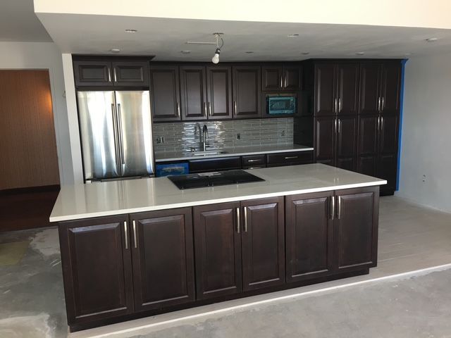 Dark wood kitchen with island, stainless steel appliances, and light countertops in a room under construction.