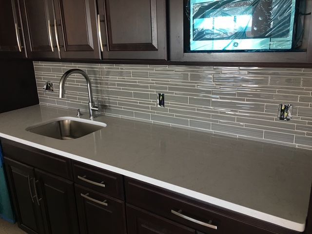 Gray countertop and backsplash with a stainless steel sink and faucet in a dark-brown cabinet kitchen.