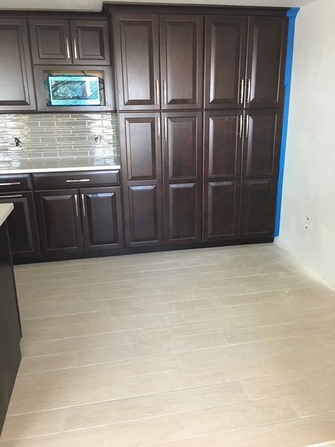 Kitchen with dark brown cabinets, light wood-look floor, beige tile backsplash; mostly empty space.