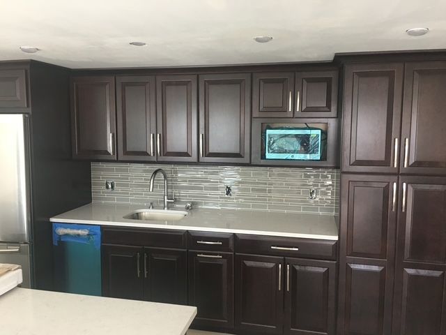 Dark wood kitchen cabinets above and below a white countertop with a sink and tile backsplash.