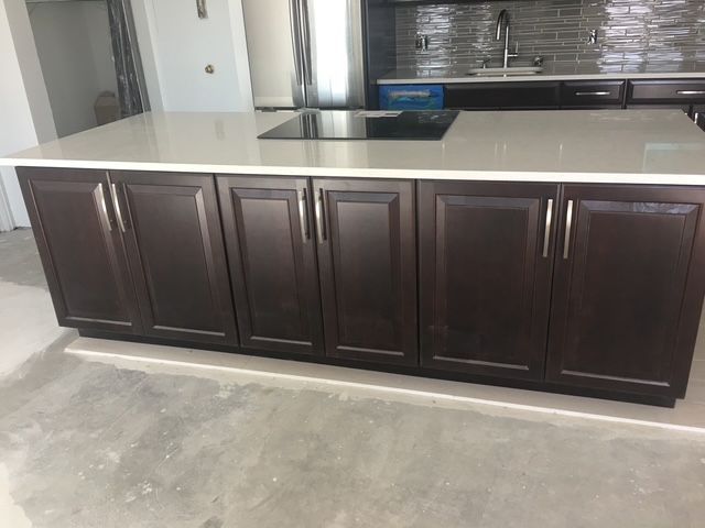 Kitchen island with dark cabinets, light countertop, and a cooktop.