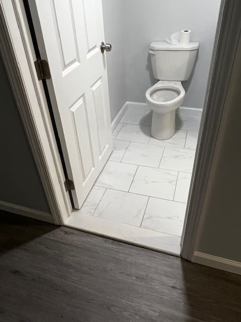 A small, tiled bathroom with a white toilet, open white door, and gray walls.