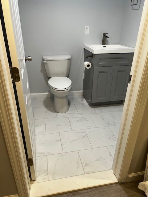 Bathroom with white toilet, gray vanity, and white tiled floor.