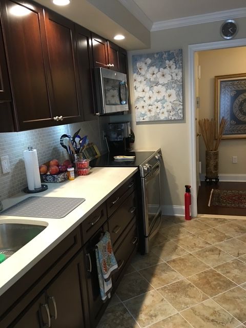 Kitchen with dark cabinets, light countertops, and tile floor. Artwork on the wall, open doorway.