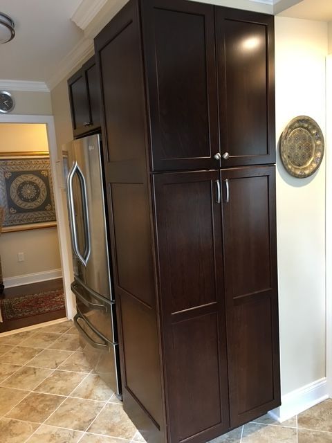 Dark brown pantry cabinet next to a stainless steel refrigerator in a kitchen.