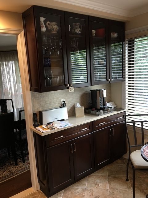Dark brown kitchen cabinets with light countertop, coffee maker, and blinds.