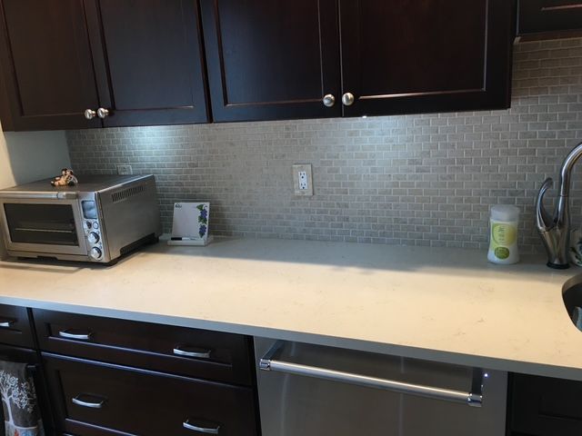 Kitchen with dark brown cabinets, light counter, tiled backsplash, and stainless steel appliances.