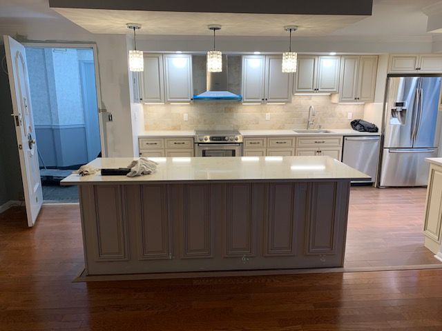 Newly renovated kitchen with light gray cabinets, white countertops, island, and stainless steel appliances.