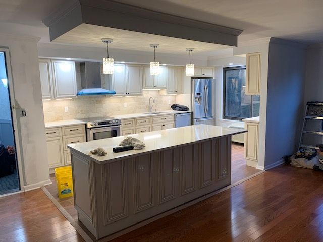 Newly renovated kitchen with a large island, light cabinets, and a stainless steel refrigerator.