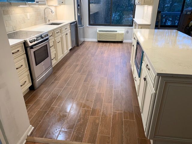 Kitchen with cream cabinets, stainless steel appliances, and wood-look tile flooring. Island and window present.