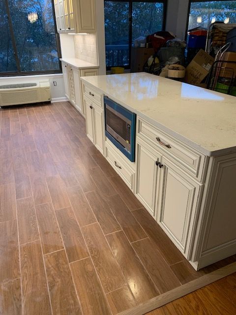 A bright, newly renovated kitchen with a large white island, wood-look tile floor, and a microwave.