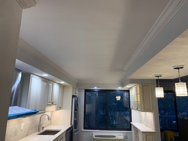 Kitchen with white cabinets, countertops, and crown molding. A large window and pendant lights are visible.