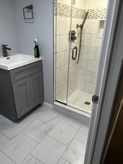 Bathroom with gray vanity, tiled floor/shower, glass shower door, and a silver faucet.