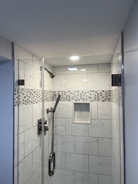 Shower with glass doors, white tile, decorative band of small mosaic tiles.