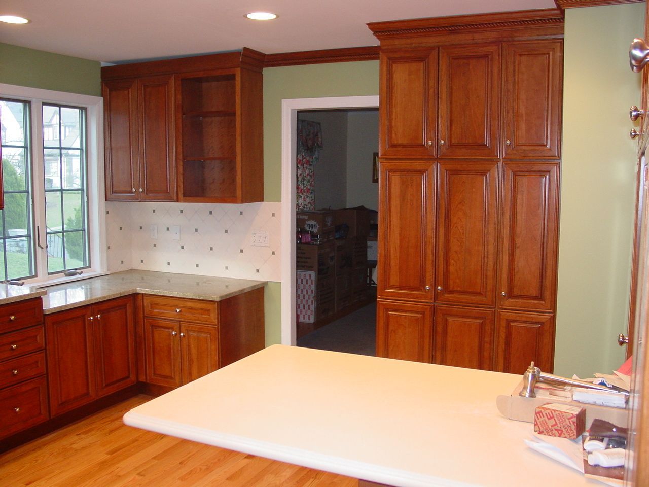 Kitchen with cherry wood cabinets, white countertops, green walls, and a doorway to a hallway.