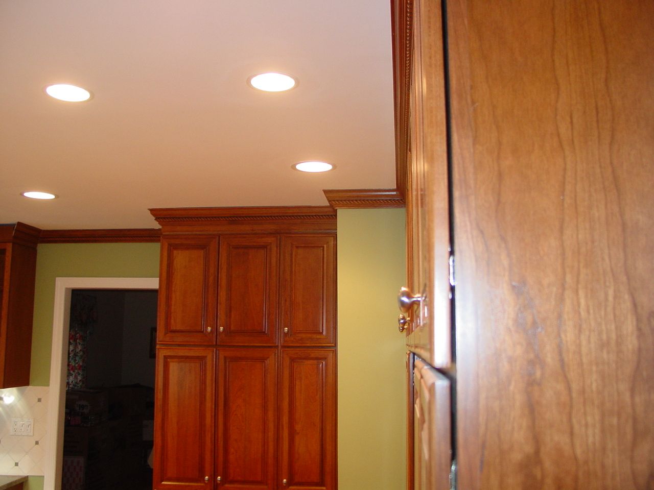 Kitchen with cherry-colored cabinets, recessed lights, and green wall.