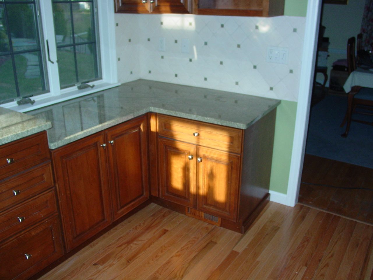 Wooden kitchen cabinets with a granite countertop near a window and light-colored hardwood floor.