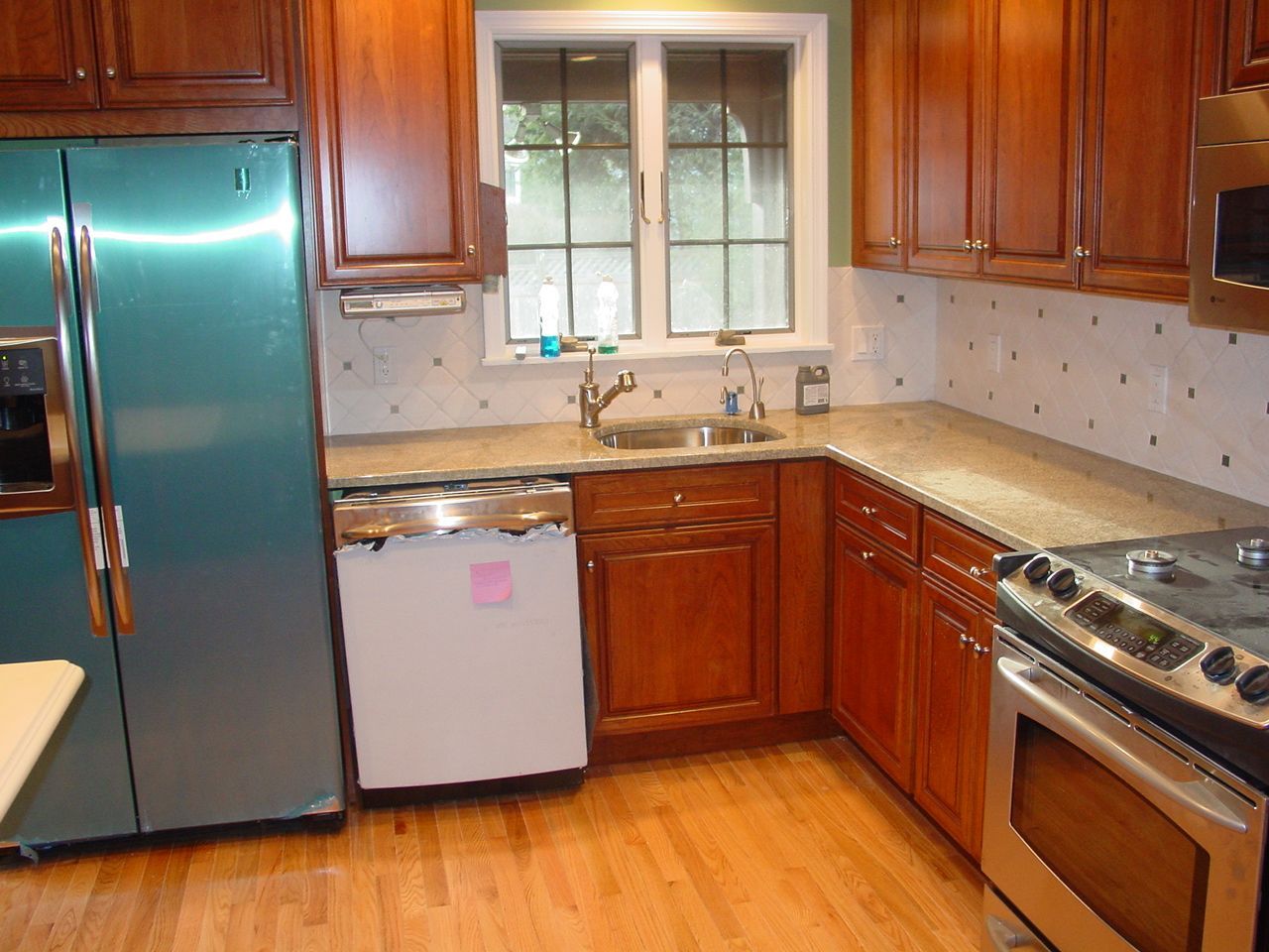 Kitchen with teal refrigerator, wood cabinets, sink, and stainless steel oven.