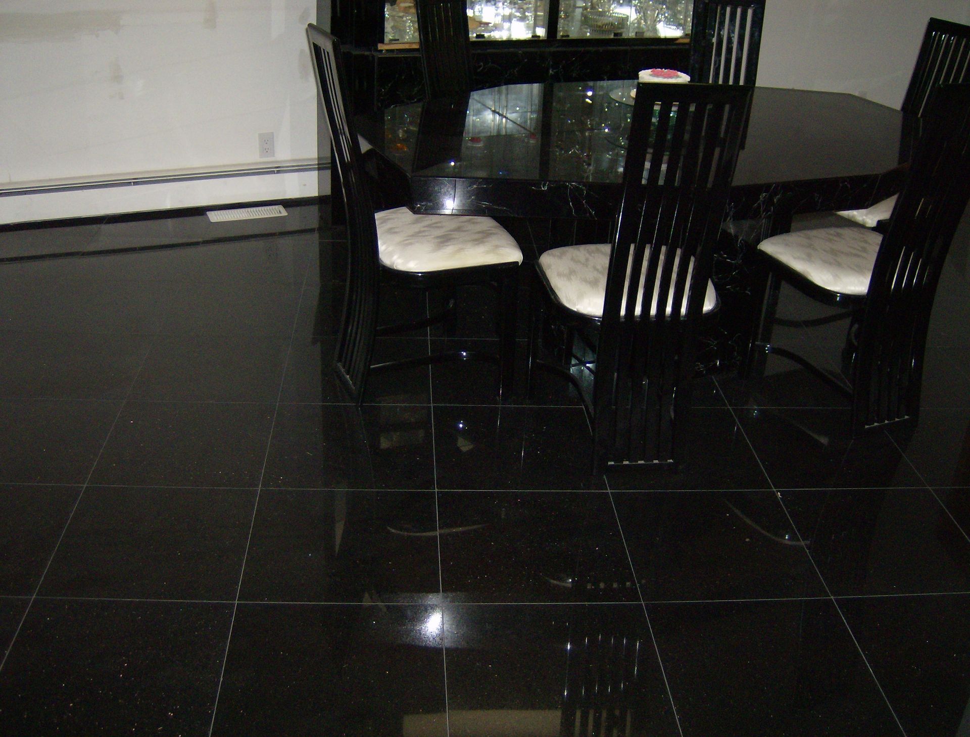 Black tiled floor reflecting a black dining set with white cushions in a room with a window.