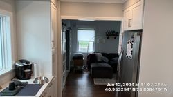 Kitchen with white cabinets, stainless steel refrigerator, and doorway to living room with couch and window.