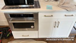 Built-in oven and microwave in a white kitchen cabinet with gold handles.
