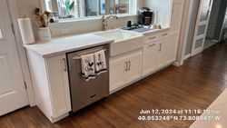 Kitchen with white cabinets, stainless steel dishwasher, farmhouse sink, window, and wooden floors.