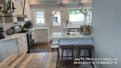 A bright kitchen with white cabinets, a center island, and a wooden dining table. Two bar stools are in front of the island.