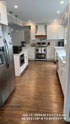 Modern white kitchen with stainless steel appliances, wooden floor, and a central island.