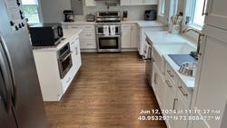 Spacious white kitchen with stainless steel appliances, brown wood floors, and a large window.