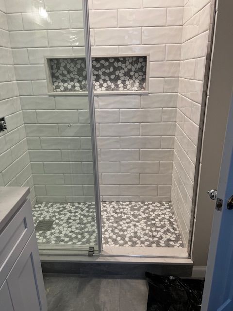 A tiled shower with a glass door, a mosaic floor, and a recessed shelf.