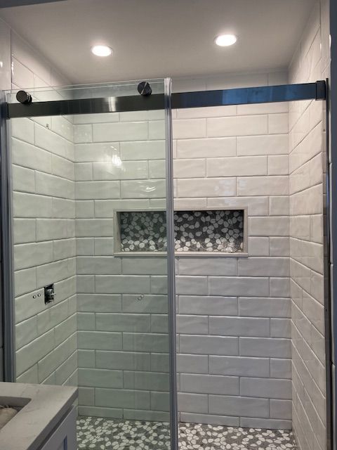 Modern shower with sliding glass doors, white brick-like tiles, and mosaic floor. Recessed shelf with mosaic tile.