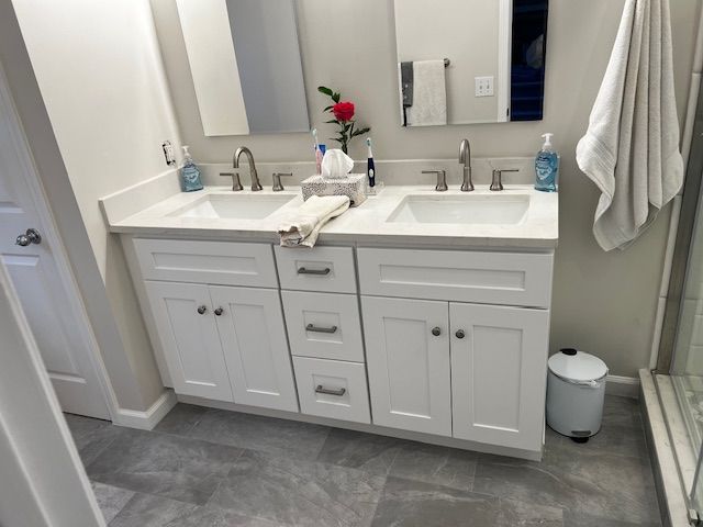 White double vanity with gray countertops, sinks, and chrome faucets. Gray tiled floor.