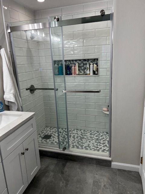 Modern bathroom with a glass-enclosed shower, white subway tile, and gray and white patterned floor.
