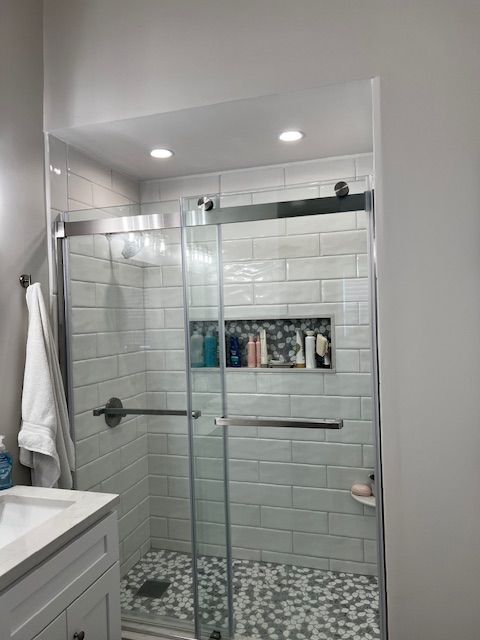 Bathroom with a glass shower, white subway tile, mosaic floor, and built-in shelf.