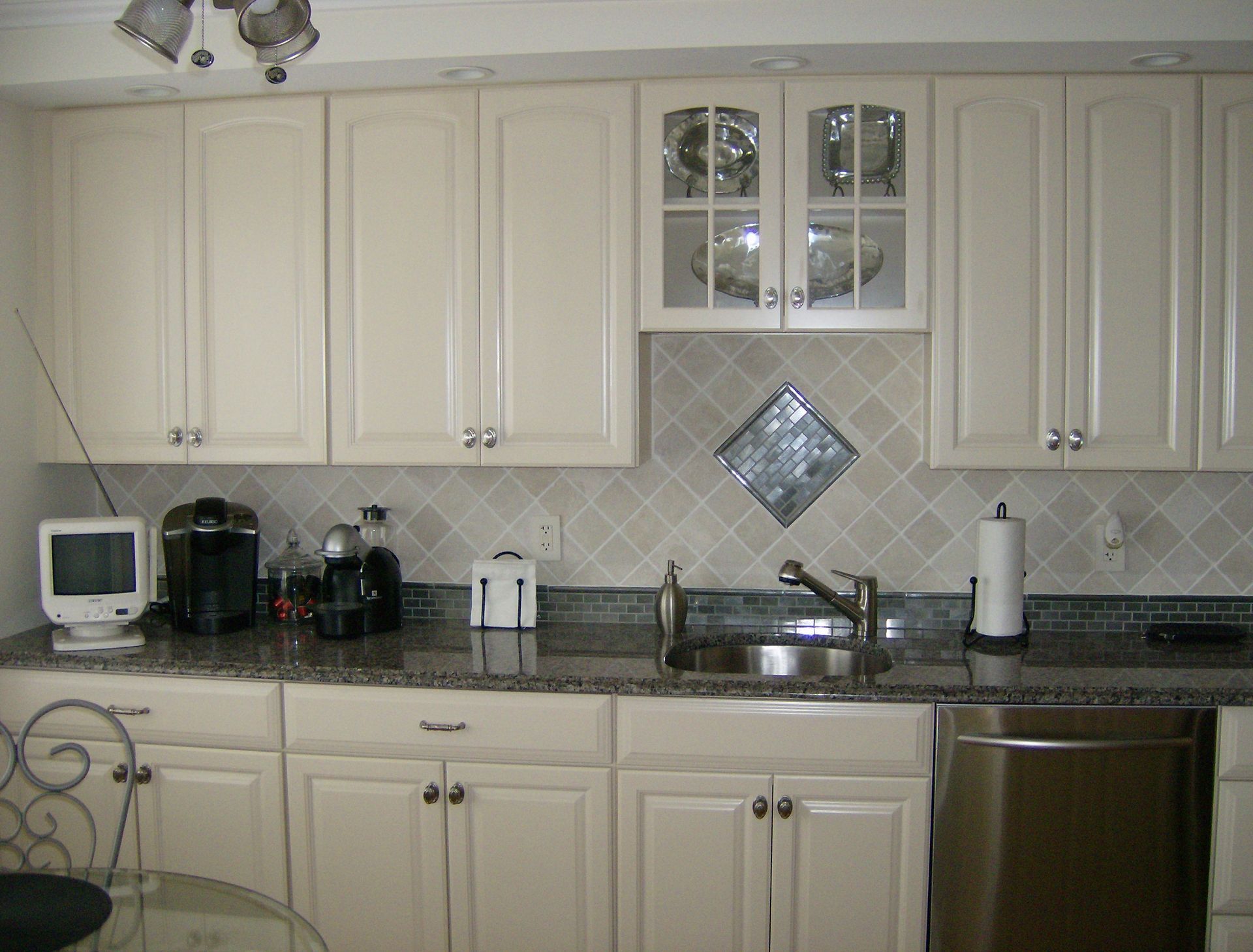 Cream-colored kitchen cabinets with a granite countertop, stainless steel sink and appliances.