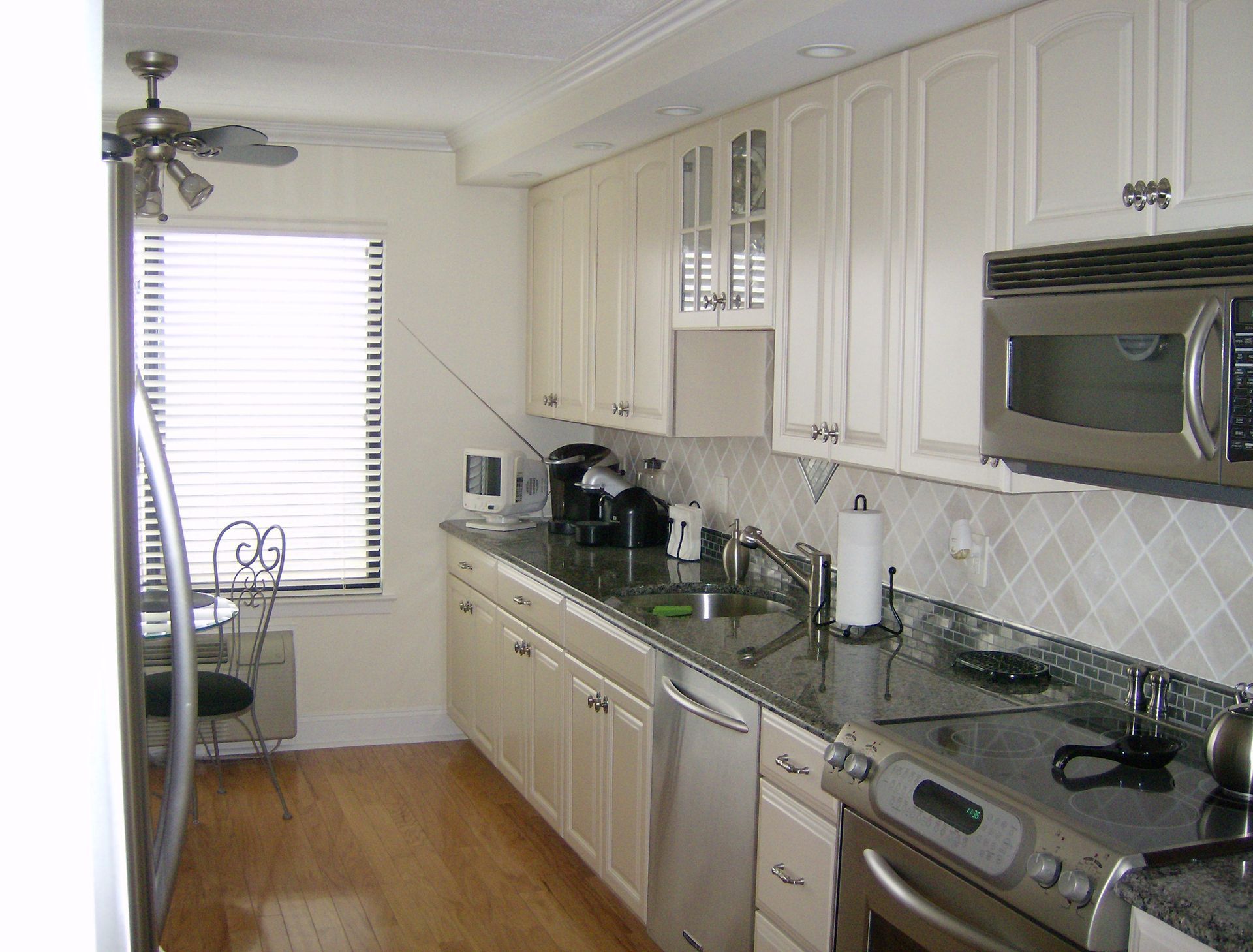 Kitchen with white cabinets, stainless steel appliances, and a window with blinds.
