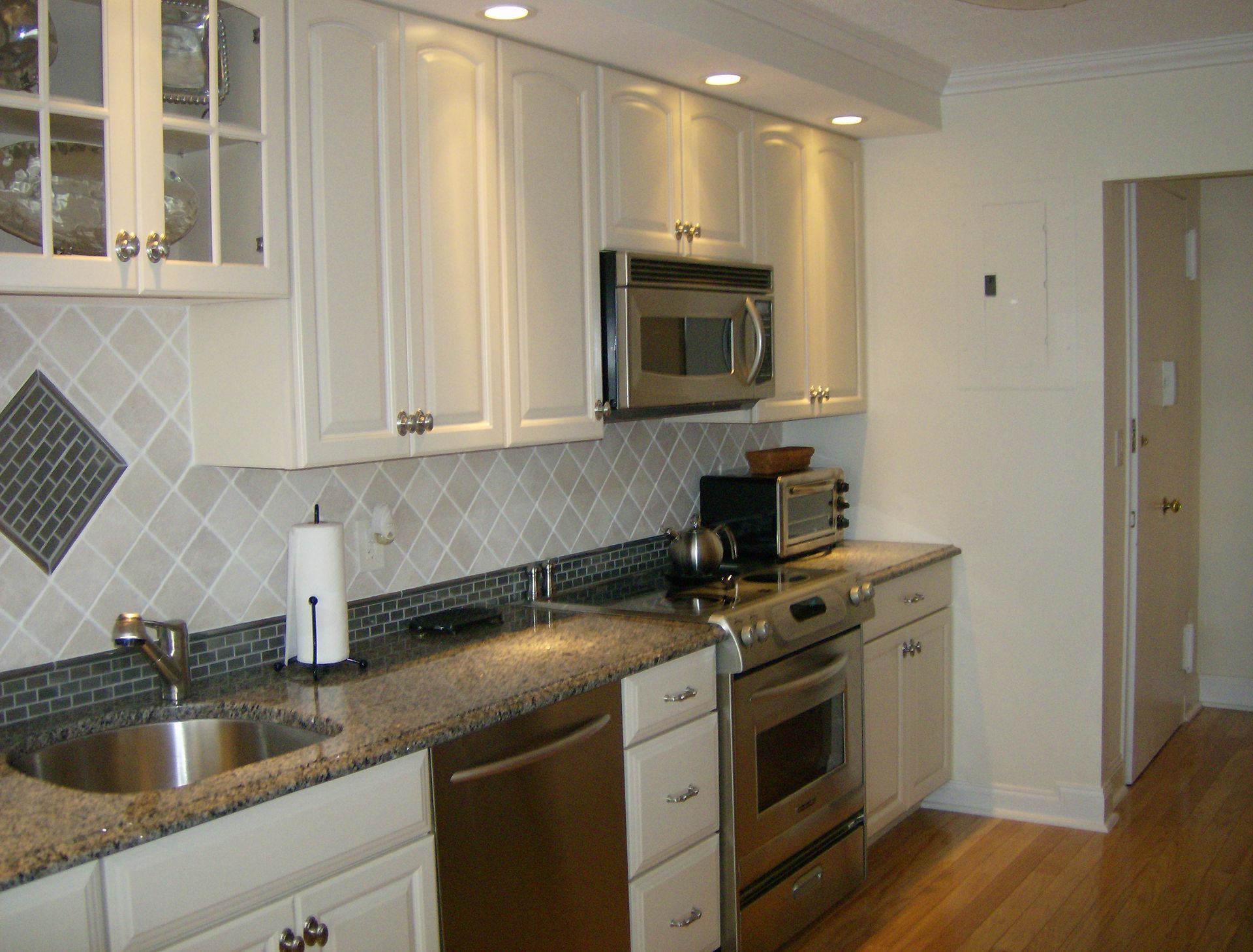 Small kitchen with white cabinets, stainless steel appliances, and a patterned backsplash.