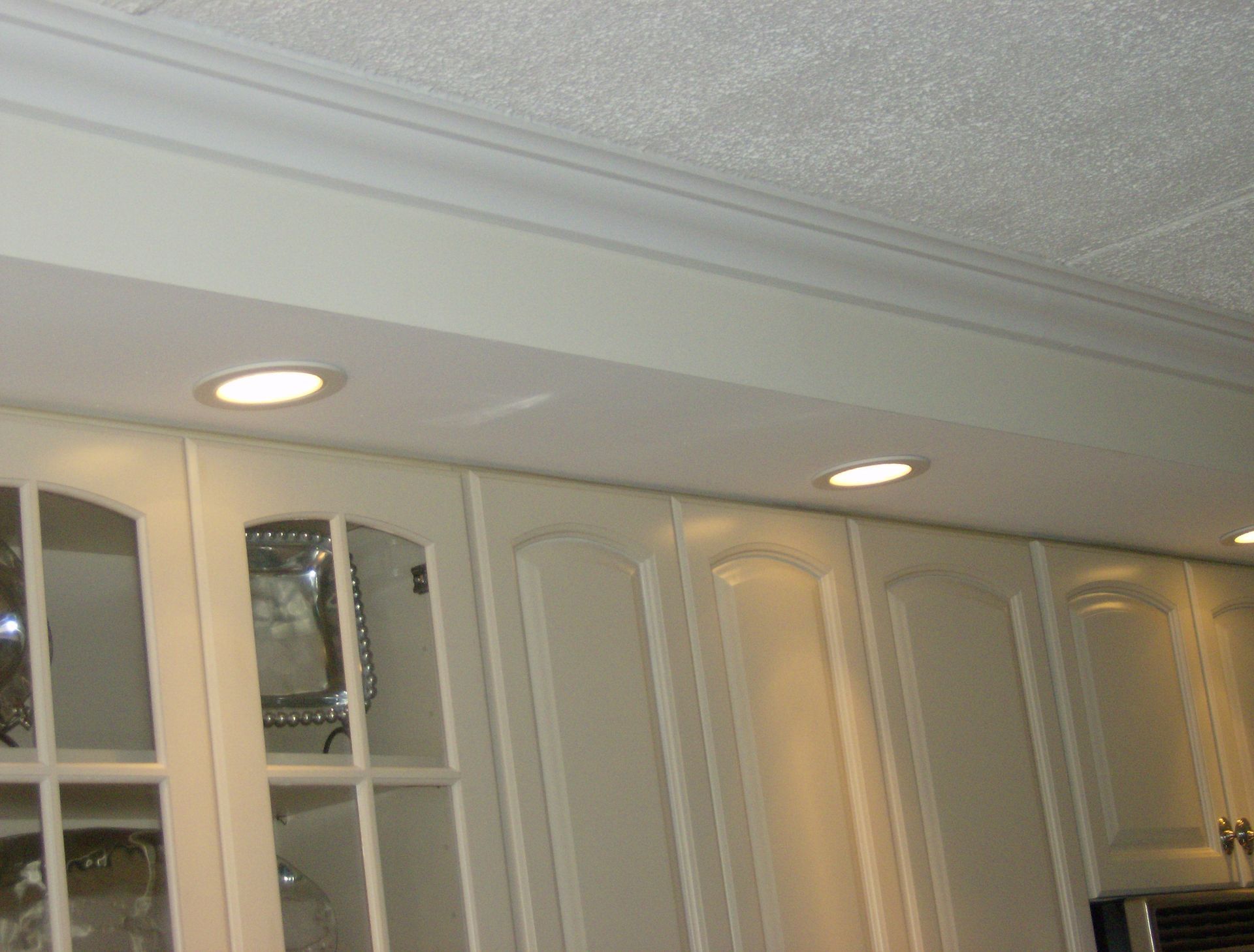 Cream-colored kitchen cabinets with recessed lighting and crown molding against a textured white ceiling.