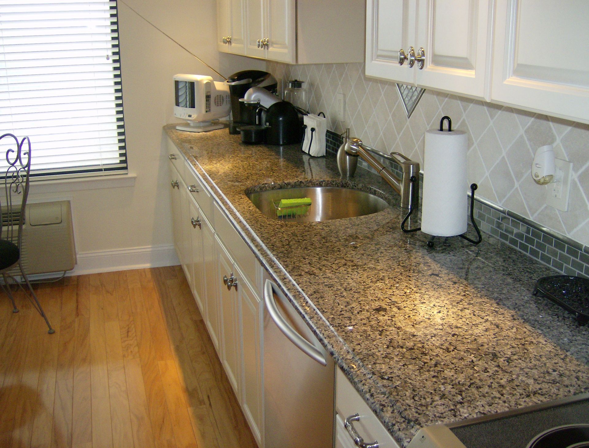 A kitchen with white cabinets, a granite countertop, stainless steel sink and appliances, and wood floor.