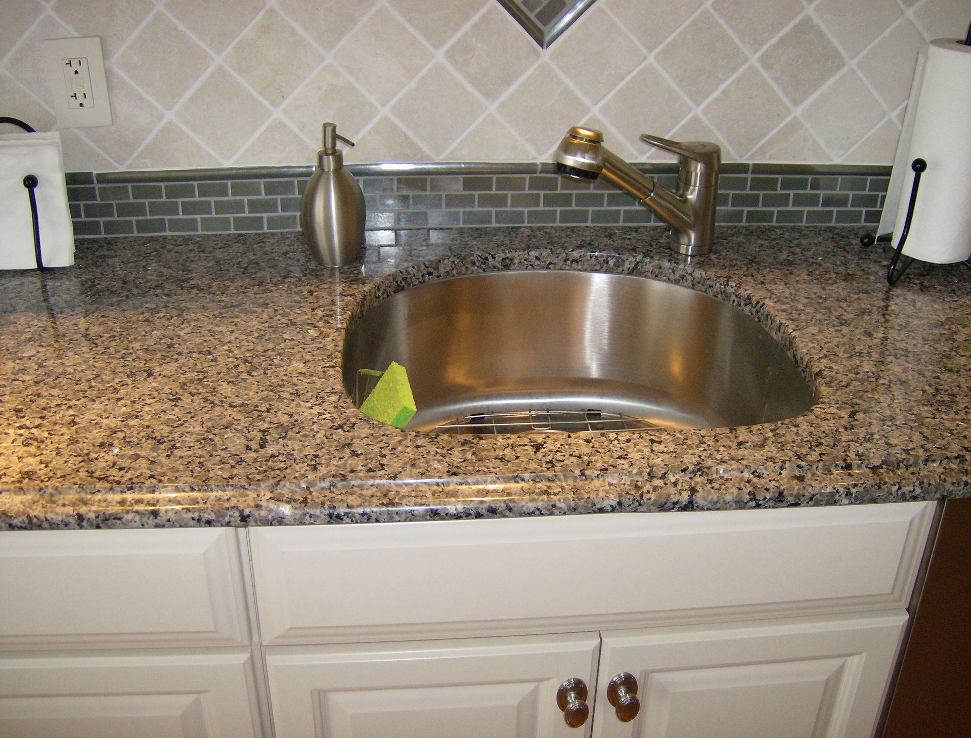 Kitchen sink with stainless steel basin, granite countertop, and white cabinets.