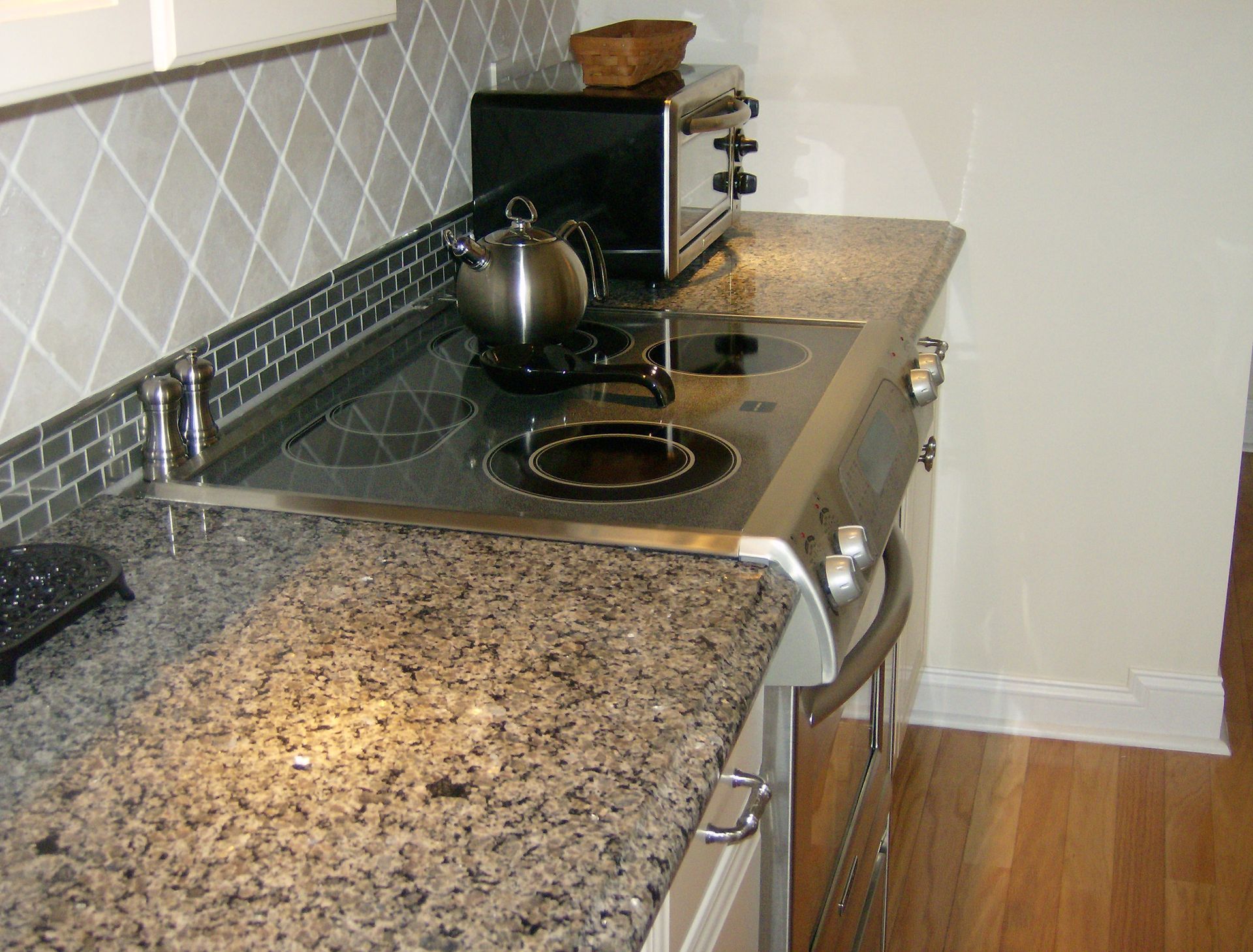Kitchen countertop with stovetop and stainless steel appliances, wood floor, tile backsplash.