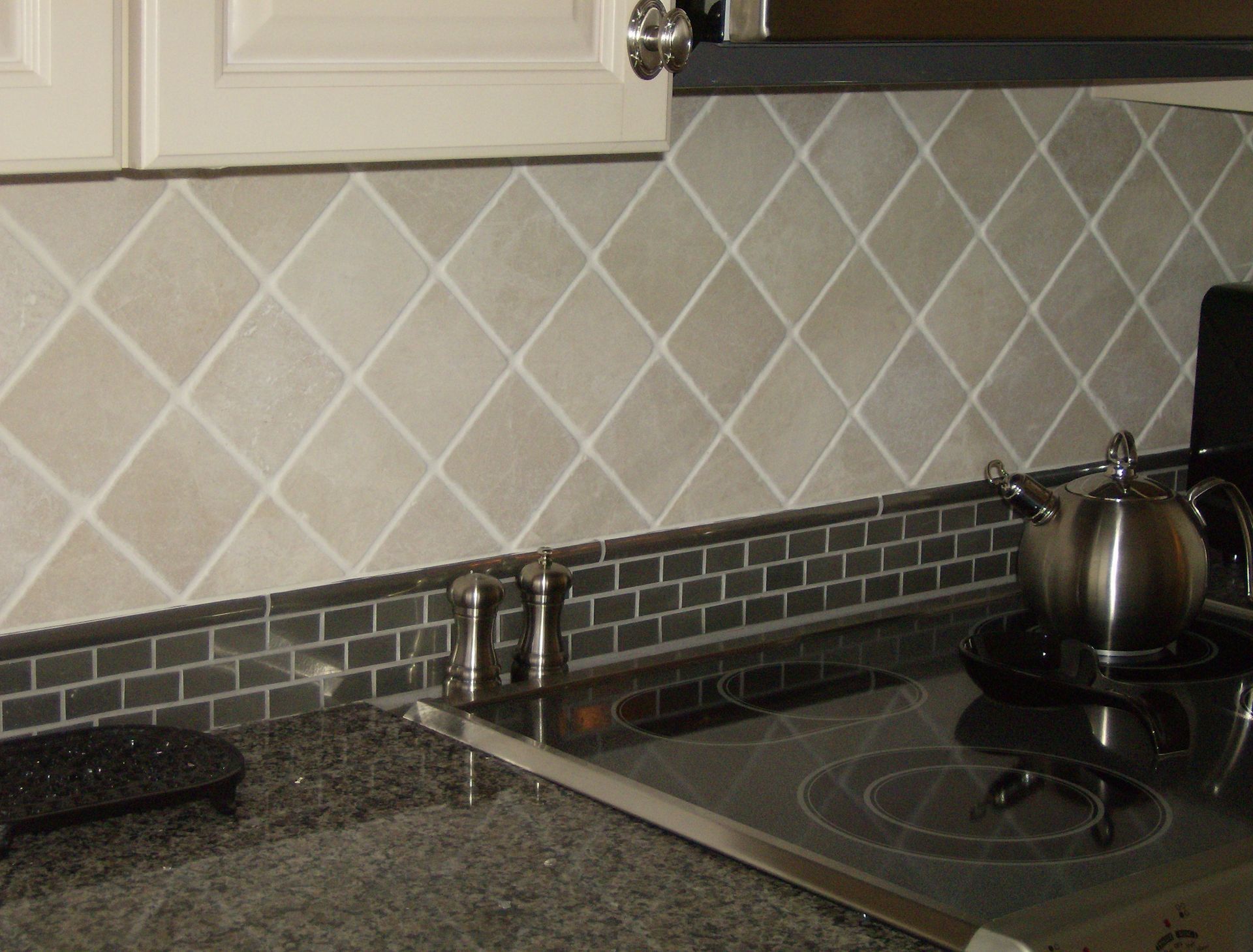 Kitchen with light-beige diamond-patterned tile backsplash and dark-gray countertop and cooktop.