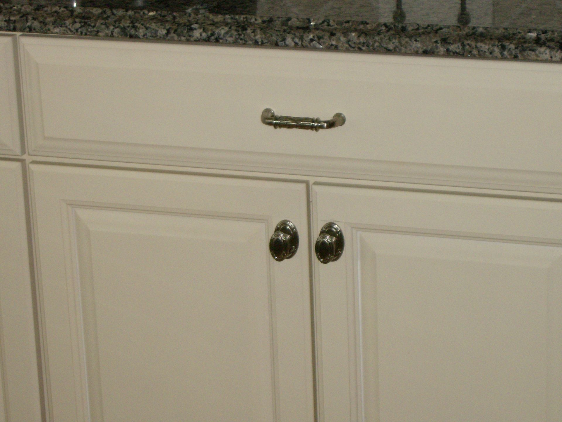 White kitchen cabinets with silver hardware and granite countertop.
