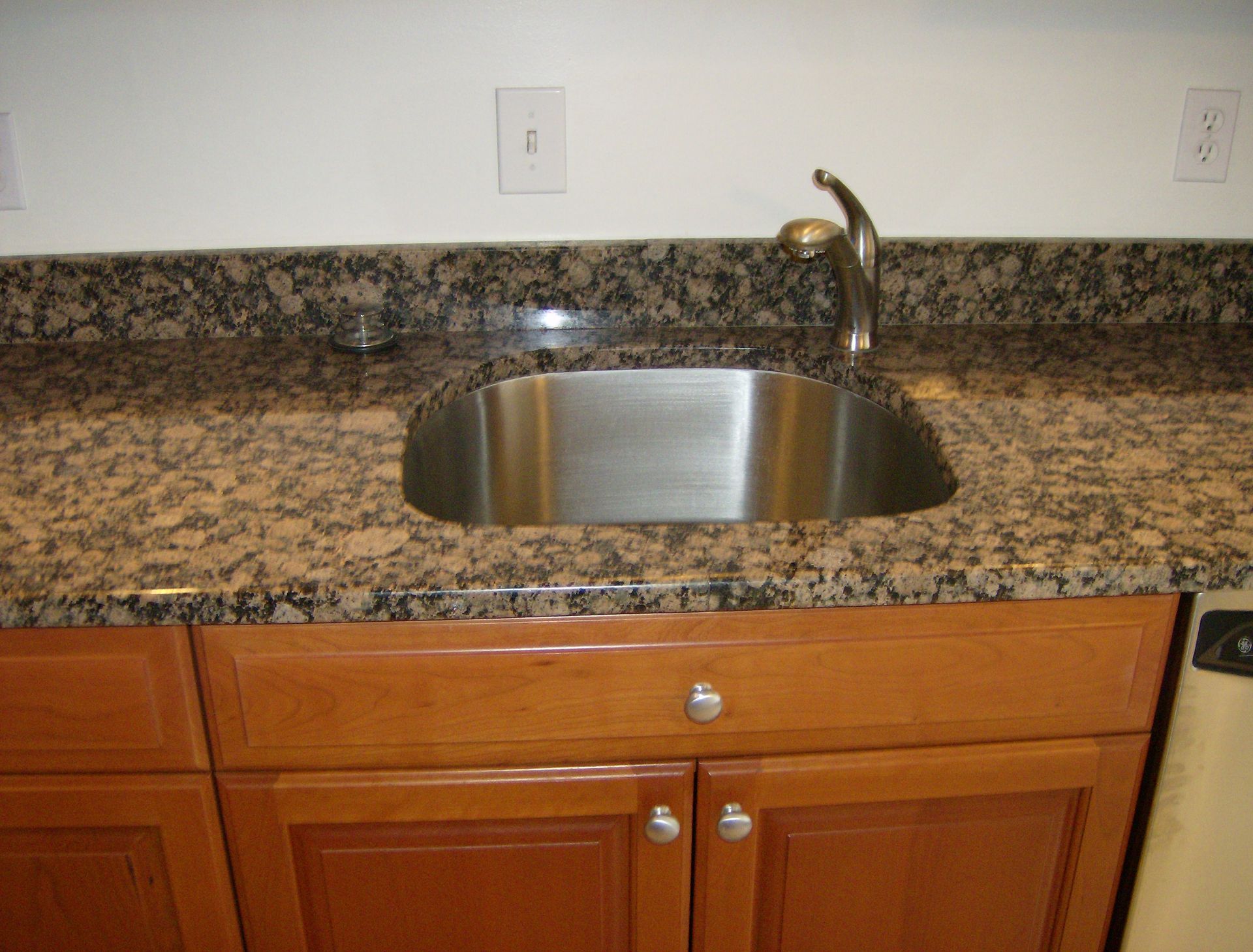 Kitchen sink with granite countertop, wooden cabinets, and a faucet.