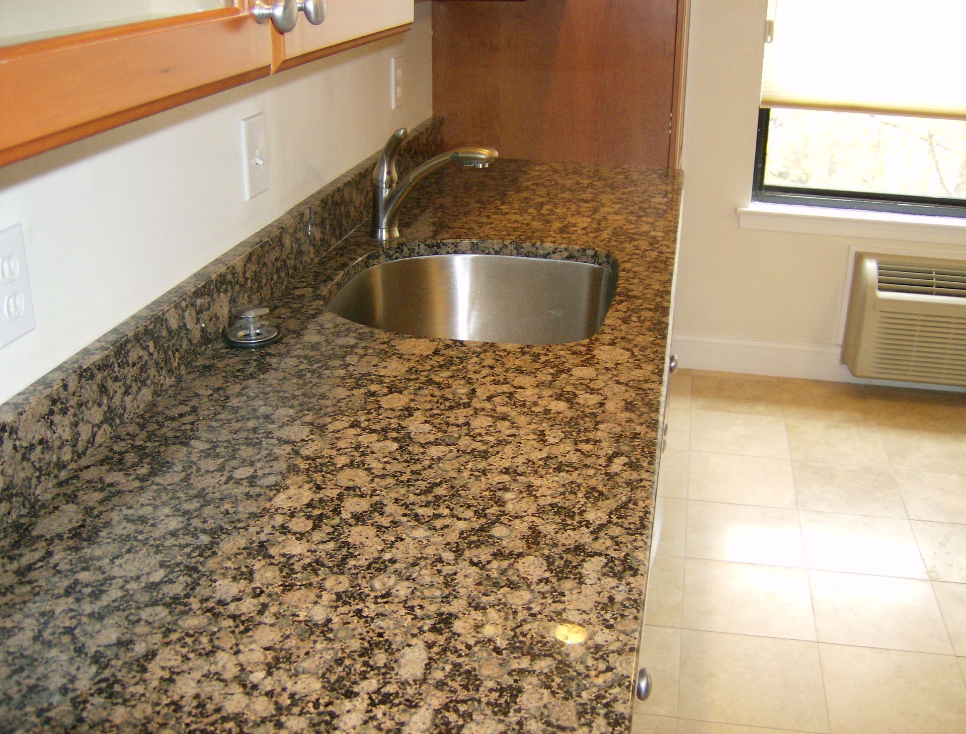 Granite countertop with stainless steel sink in a kitchen, beige tile floor.